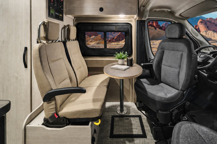 Modern RV rental interior: comfortable swivel seats, dining table, and a scenic desert window view for your road trip adventures.