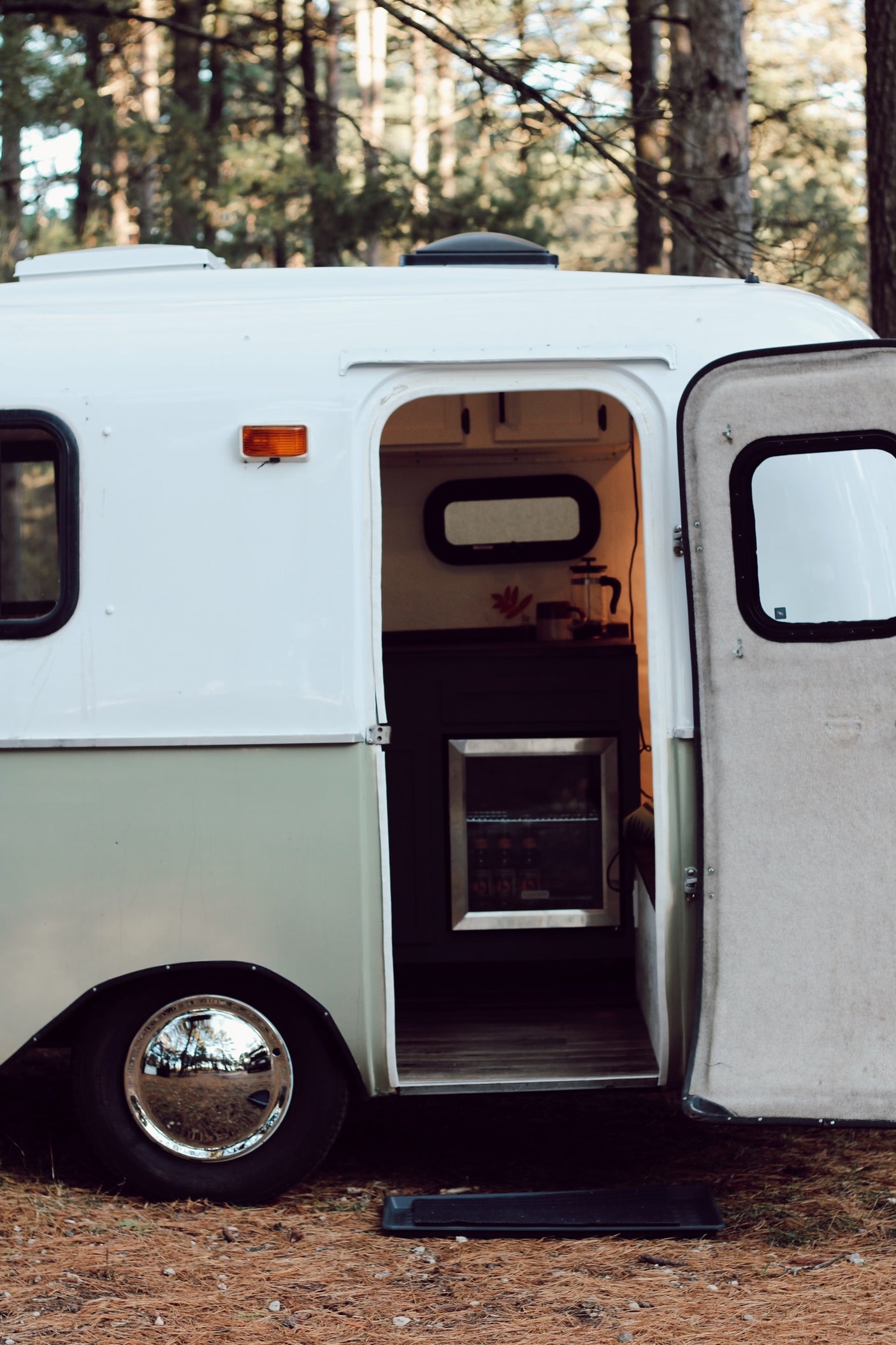 Cozy RV rental in the forest with an open door showing the interior kitchenette. Perfect for glamping.