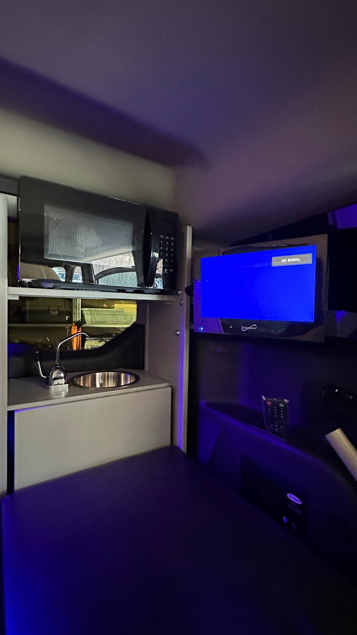 Night-lit RV rental interior featuring a compact kitchenette (microwave, sink), TV (no signal), and bed area, ideal for camping. — photo 6