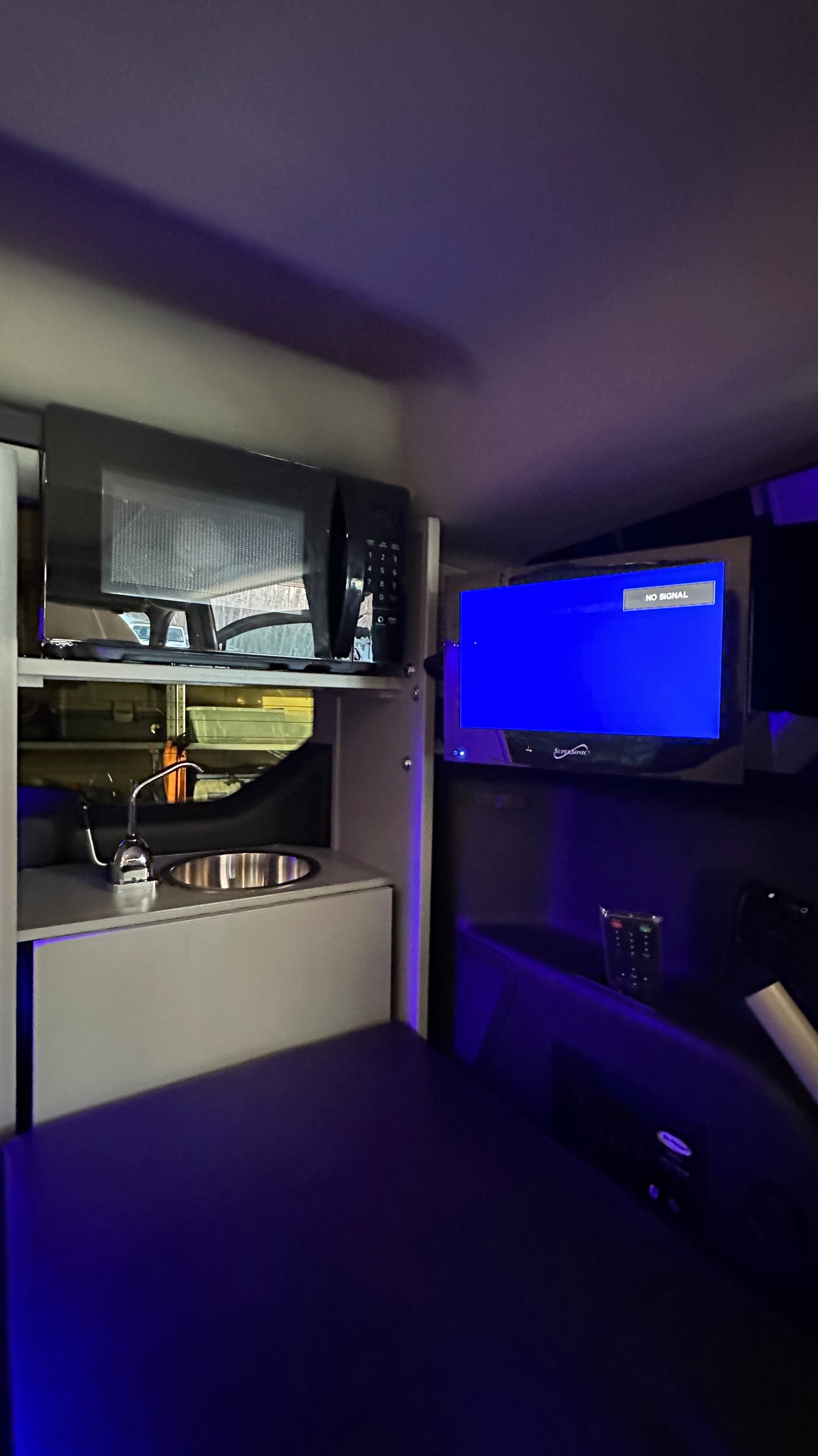 Night-lit RV rental interior featuring a compact kitchenette (microwave, sink), TV (no signal), and bed area, ideal for camping.