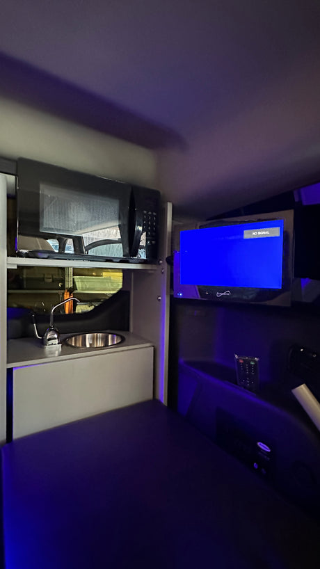 Night-lit RV rental interior featuring a compact kitchenette (microwave, sink), TV (no signal), and bed area, ideal for camping.