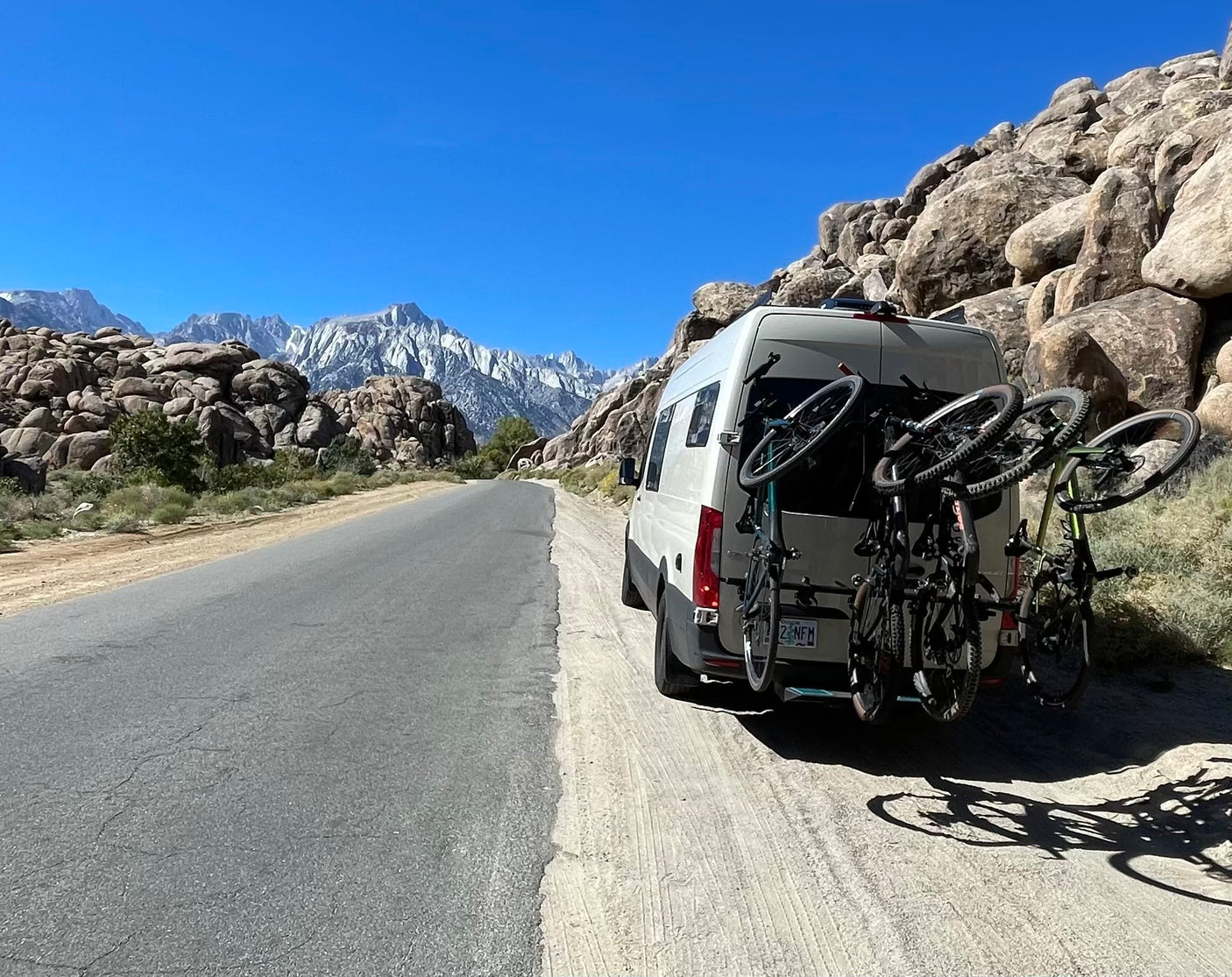 RV rental van with bikes parked on dirt shoulder, facing majestic Sierra Nevada mountains & unique rock formations.