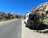 RV rental van with bikes parked on dirt shoulder, facing majestic Sierra Nevada mountains & unique rock formations.