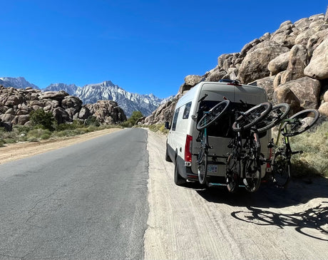 RV rental van with bikes parked on dirt shoulder, facing majestic Sierra Nevada mountains & unique rock formations.