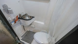 Inside an RV rental: a compact bathroom with toilet, sink, shower, hand sanitizer, and floor mat for comfort.