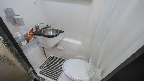 Inside an RV rental: a compact bathroom with toilet, sink, shower, hand sanitizer, and floor mat for comfort.
