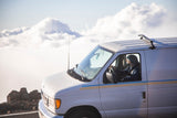 White RV rental van high on a mountain road, with a driver looking out over a sea of clouds.