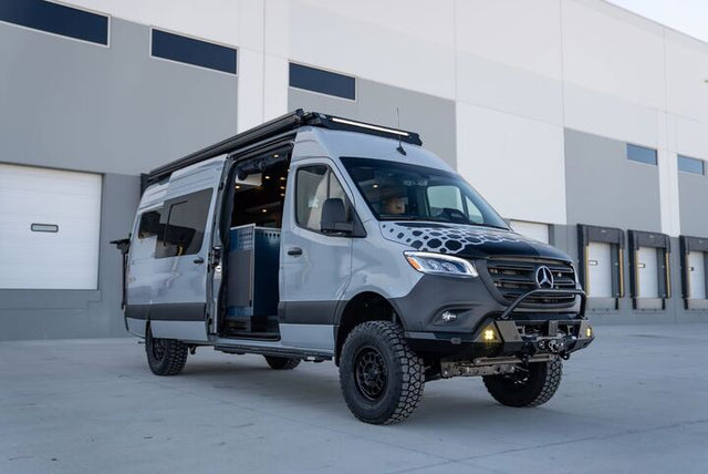 This rugged Mercedes Sprinter camper van RV rental, with off-road tires and an open side door, is ready for your next adventure.