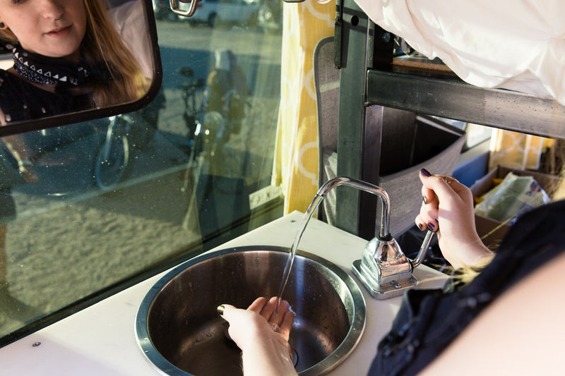 Washing hands in a compact RV rental sink with a pump faucet. User's reflection seen in the window. — photo 6