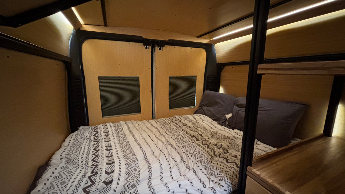 RV rental: Cozy camper van interior featuring a comfortable bed with patterned bedding, warm wood paneling, and inviting LED lighting.