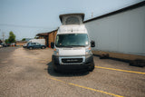 Front view of a white Ram ProMaster pop-top camper van on asphalt, perfect for your next rv rental adventure!