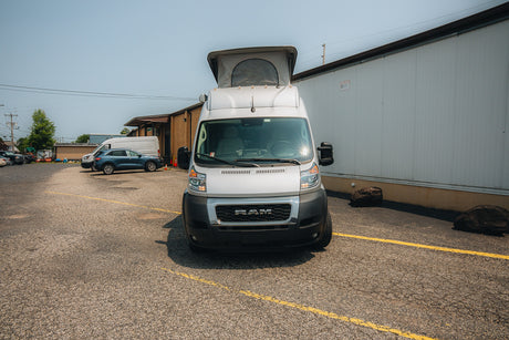 Front view of a white Ram ProMaster pop-top camper van on asphalt, perfect for your next rv rental adventure!