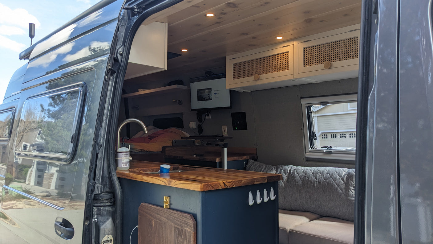 Well-equipped camper van interior seen through an open door, revealing a kitchen, living area, and comfy seating for rv rental.