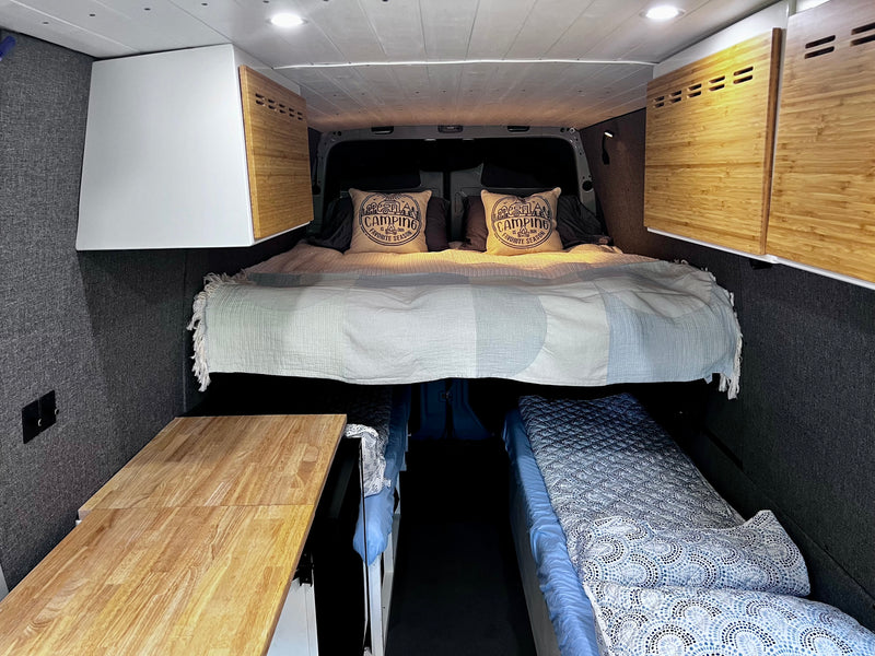 Spacious RV rental interior featuring a large rear bed, bamboo overhead cabinets, and a wooden side table setup. — photo 11