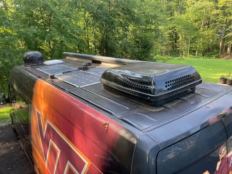 Detailed rooftop view of an RV rental, showing solar panels, an AC unit, and other travel equipment.