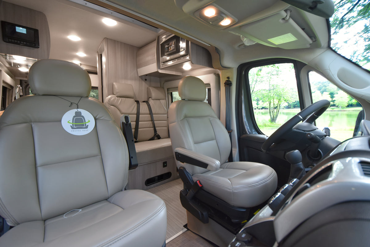 An RV rental interior showing light-colored swivel front seats, a rear bench, a microwave, and a serene lake view. — photo 9