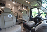 An RV rental interior showing light-colored swivel front seats, a rear bench, a microwave, and a serene lake view.
