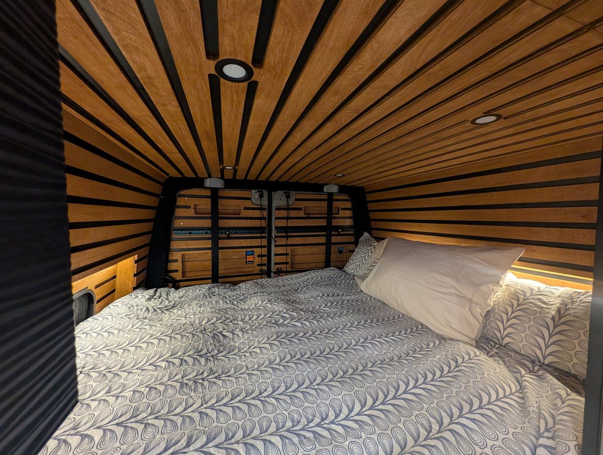Cozy RV rental interior featuring a comfortable bed with patterned bedding, warm wood paneling, and recessed lighting. — photo 17