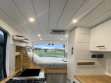 Spacious RV rental interior with a cozy bed, full kitchen, and scenic view, perfect for mobile living adventures.