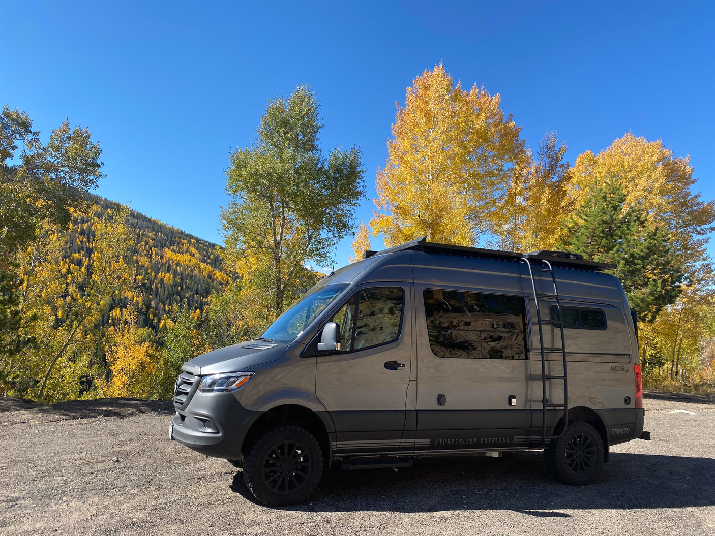 This gray Storyteller Overland Mode 4x4 Stealth camper van, ideal for rv rental, enjoys stunning fall mountain views.
