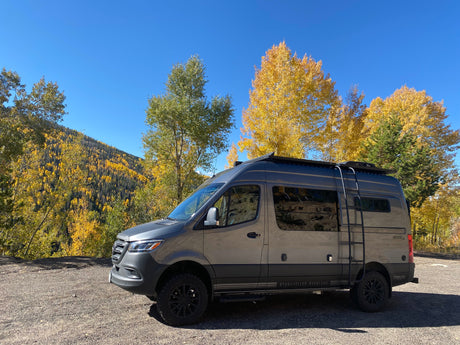 This gray Storyteller Overland Mode 4x4 Stealth camper van, ideal for rv rental, enjoys stunning fall mountain views.