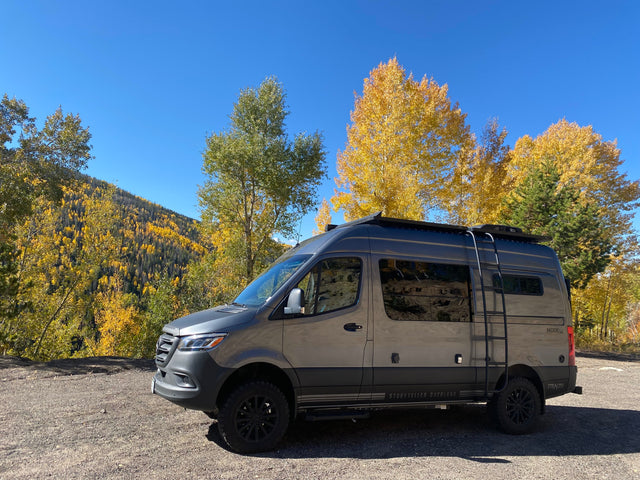 This gray Storyteller Overland Mode 4x4 Stealth camper van, ideal for rv rental, enjoys stunning fall mountain views.