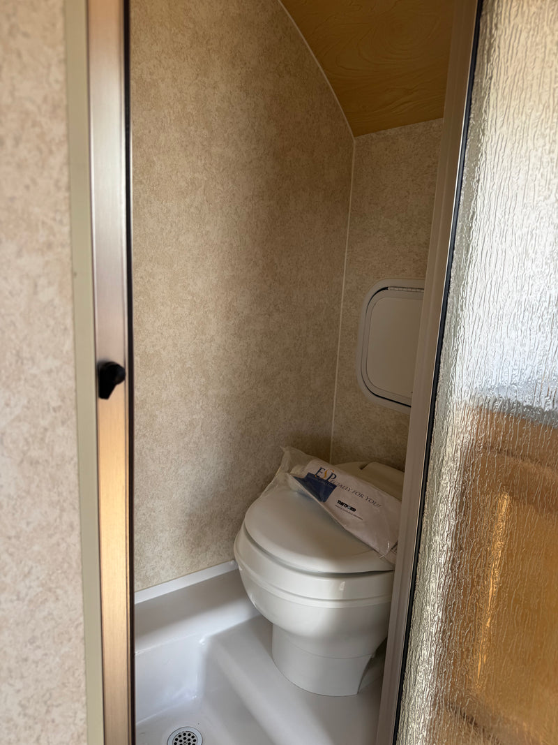 Compact RV rental wet bath with toilet inside shower stall, seen through a partially open frosted glass door. — photo 11