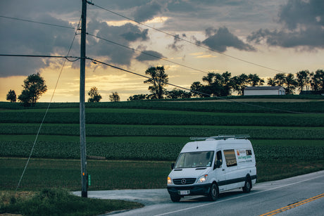 A white commercial van for solar energy drives on a rural road, passing green fields and a power pole. Perfect for an RV rental drive.