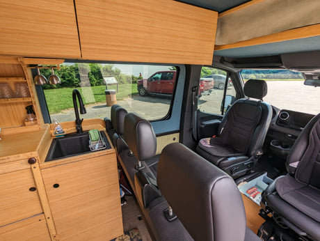 Custom-built RV rental interior with bamboo kitchen, sink, and comfy seats for your next adventure.