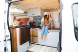 Step inside this charming RV rental! A woman relaxes in the beautifully designed camper van interior.