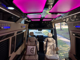 Luxury rv rental interior with plush, quilted tan seats, vibrant pink ceiling lights, and blue accent lighting, offering premium comfort.