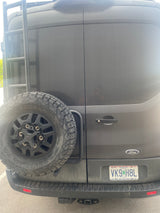 Rear view of a dark Ford Transit camper van, ideal for rv rental. Features a spare tire, ladder, and Missouri license plate.