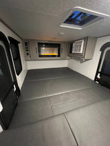 Modern RV rental interior showcasing a large comfortable bed, electric fireplace, and AC unit, ideal for travel adventures.
