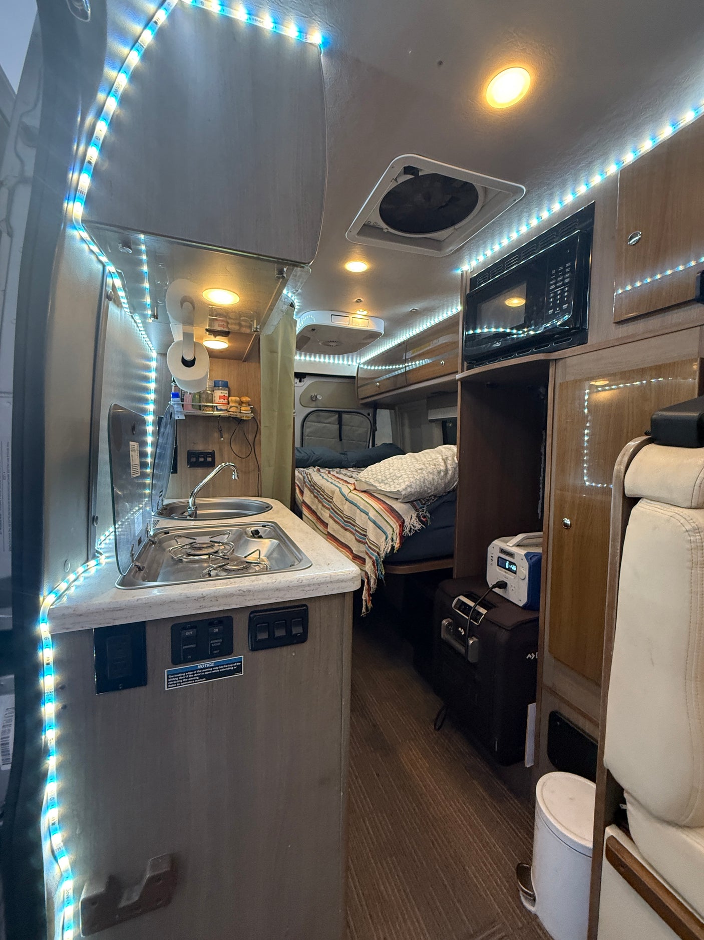Inside an RV rental, featuring a compact kitchen with stove and sink, cozy sleeping area, microwave, and bright LED lighting.