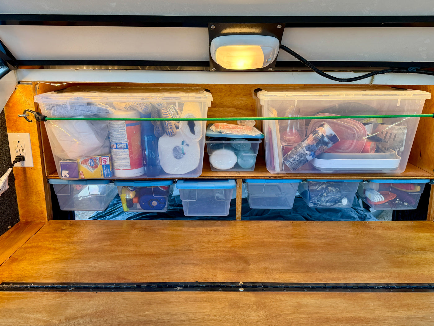 Efficient RV rental storage with clear bins, bungee cords, and an outlet, keeping essentials organized. — photo 11