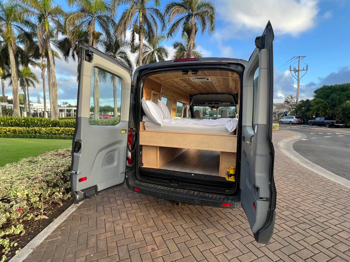 Experience van life with this rv rental! Grey camper van with open back doors revealing a wood-paneled interior, bed, and storage.