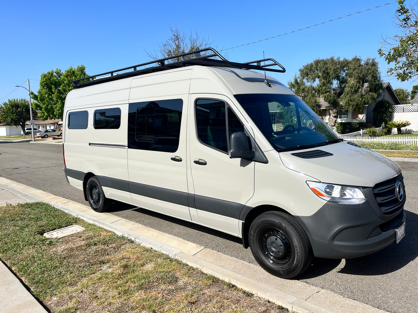 Modern light-colored Mercedes Sprinter van, equipped with a roof rack, available for RV rental.