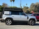 A silver Land Rover Defender with a Roofnest rooftop tent and side gear box, perfect for an adventure RV rental.