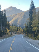 Scenic mountain road in autumn, lined with colorful trees & distant peaks. Perfect for an RV rental road trip adventure.