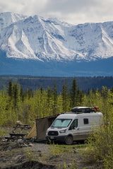 RV rental camper van set up for scenic mountain camping with an awning & picnic tables. Perfect for nature lovers.