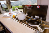 Scenic RV rental kitchen: Kettle & pan on gas stovetop, cookbook on counter, with mountain views.
