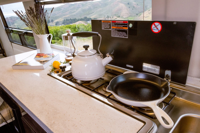 Scenic RV rental kitchen: Kettle & pan on gas stovetop, cookbook on counter, with mountain views. — photo 8
