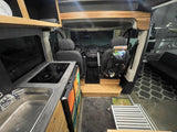 Inside a modern RV rental: view from the rear showing kitchen counter with sink & induction cooktop, and front cabin.