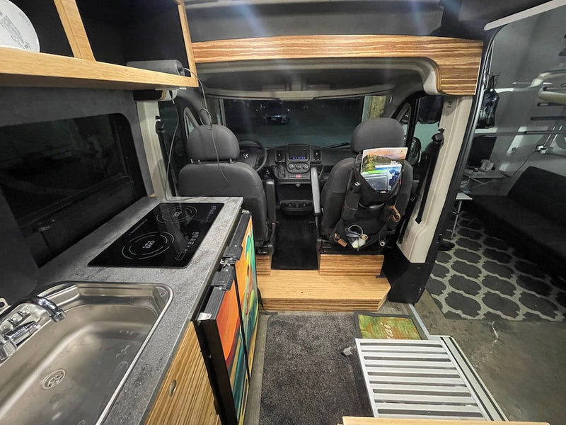  revealing interior. Ocean & sky visible.|This gray RV rental camper van is perfectly parked on a sunny sandy beach. Its side door is open — photo 6