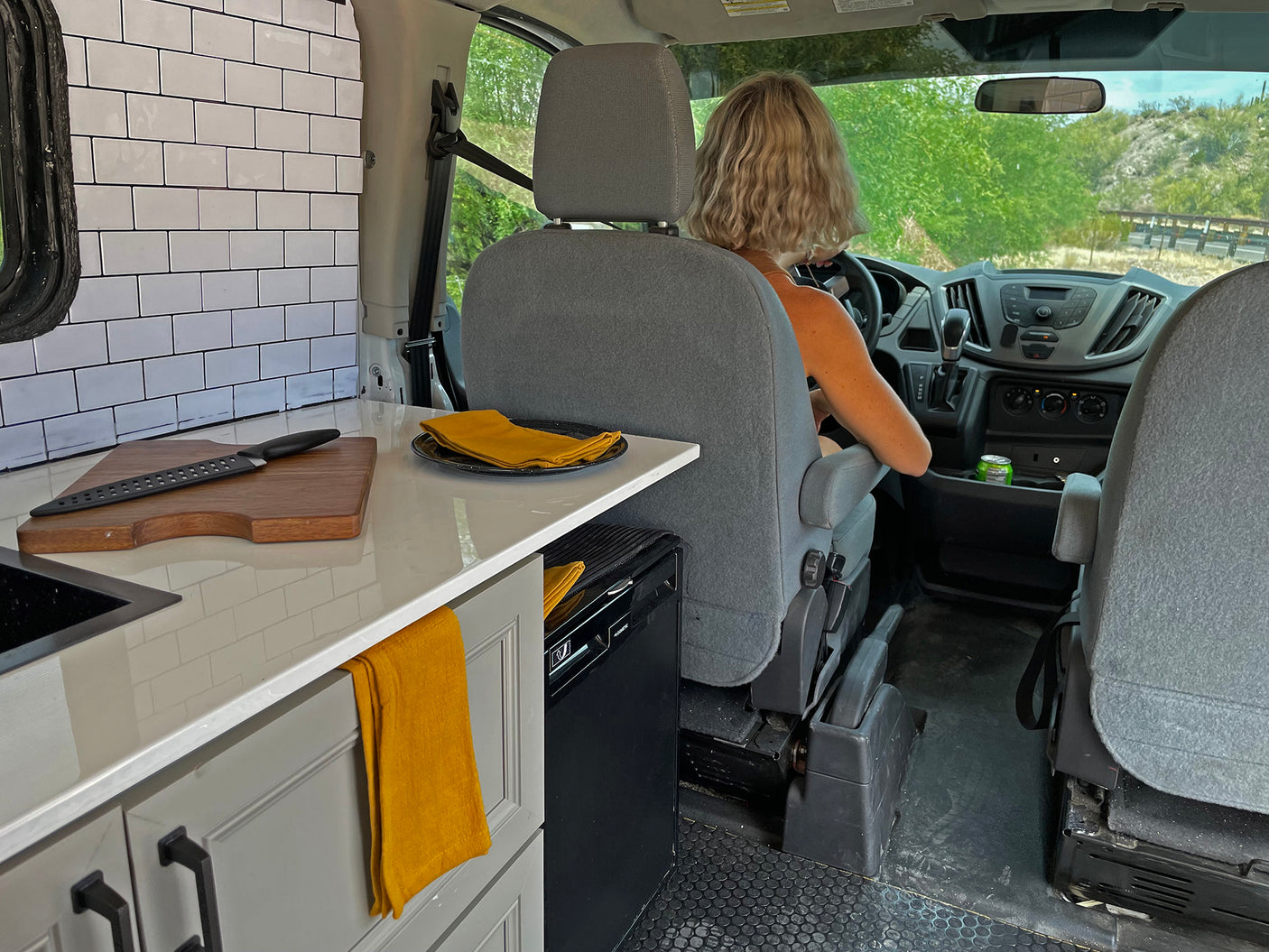 Inside this rv rental, a driver navigates a custom van with a compact kitchen, perfect for mobile living and travel.