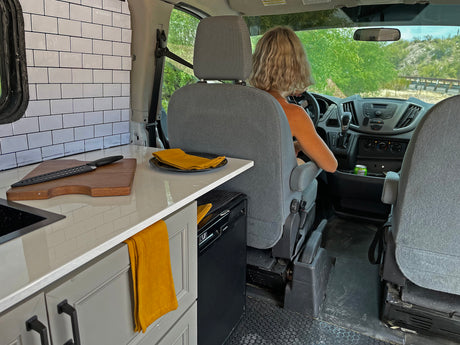 Inside this rv rental, a driver navigates a custom van with a compact kitchen, perfect for mobile living and travel.