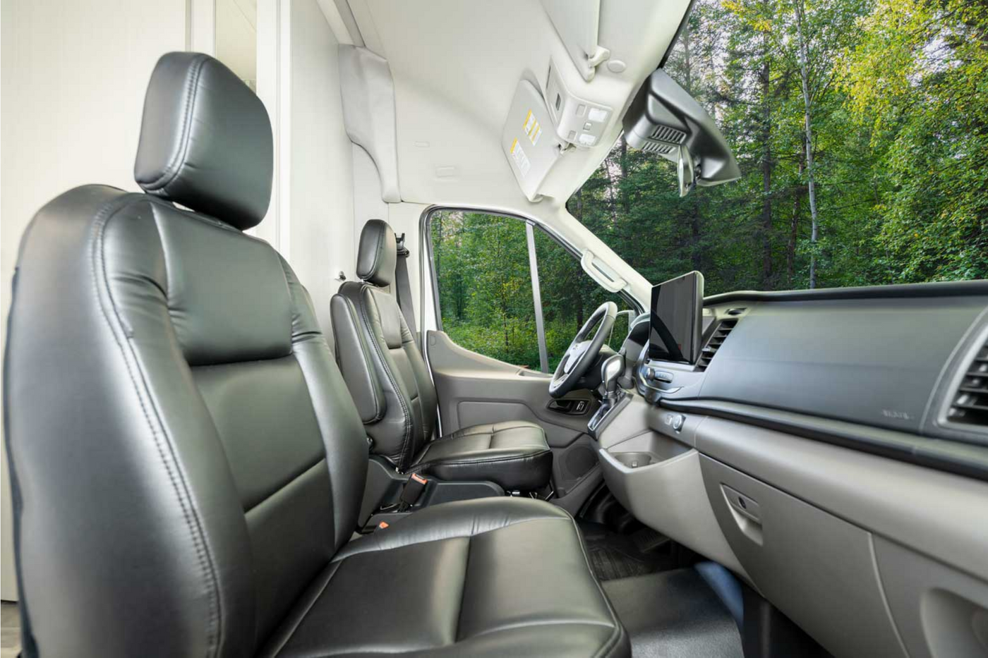 Spacious front cabin of a modern RV rental van. Black leather seats, dashboard, and forest view for your next adventure. — photo 11