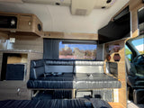 Spacious rv rental interior showing plush black leather seating/bed, large TV, and kitchen area with microwave.