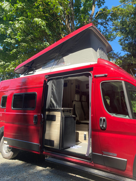 Bright red Winnebago camper van with pop-top roof open, side door revealing interior. Ideal for an RV rental experience.