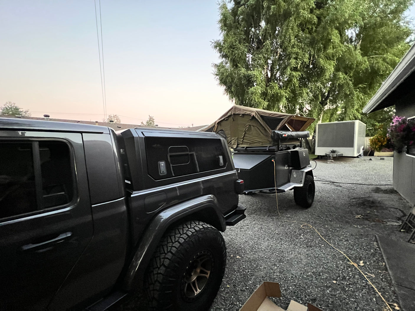 Dark truck with an overland trailer and rooftop tent deployed, a complete setup for an rv rental adventure.